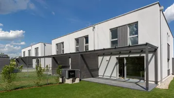 Moderne Reihenhäuser mit privatem Garten und überdachter Terrasse unter blauem Himmel.
