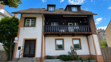 Traditionelles Haus mit weißer Fassade, Holzbalkon und Dachgauben.