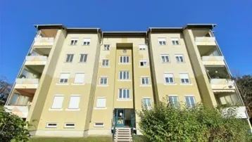 Mehrfamilienhaus mit mehreren Balkonen und gepflegter Grünfläche vor dem Eingangsbereich.