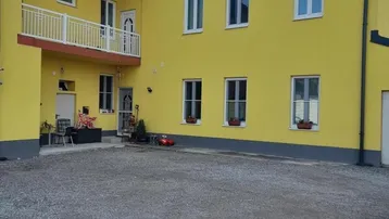 Gelbes Gebäude mit weißem Balkon und Schotterfläche davor unter blauem Himmel.