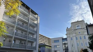 Ansicht eines Mehrfamilienhauses mit zahlreichen Balkonen und umliegenden Gebäuden an einem sonnigen Tag.