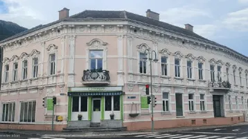 Historisches Eckgebäude mit Stuckfassade und Balkon in bergiger Umgebung.