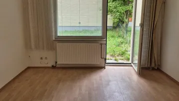 Helles Zimmer mit Laminatboden, Heizkörper und direktem Zugang zum Gartenbereich.