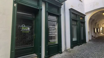 Historische Gasse mit Kopfsteinpflaster und dunkelgrünen Ladenfronten in einem alten Gebäude.