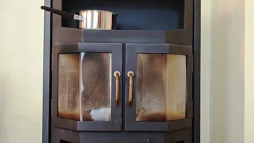 Moderner Holzofen mit schwarzem Metallgehäuse und sichtbarem Ofenrohr, der Wärme spendet.