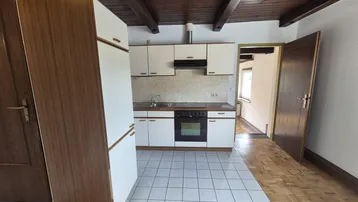 Küche mit weißen Einbauschränken, Herd und Kühlschrank, kombiniert mit Fliesen- und Parkettboden.