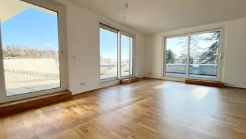 Helles, leeres Zimmer mit großen Fenstern und Holzboden, bietet Zugang zu einer Terrasse.