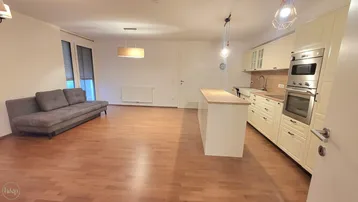 Heller offener Wohn-Essbereich mit integrierter Küche, Holzboden und Zugang zum Balkon.