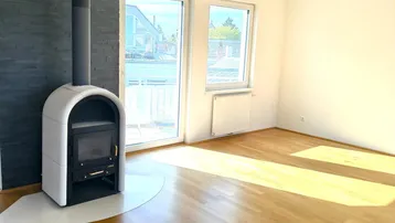 Helles Wohnzimmer mit modernem Kaminofen, Holzboden und Zugang zum Balkon.