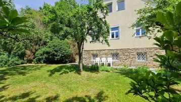Hausfassade mit Steinsockel und gepflegtem Gartenbereich mit Sitzgelegenheiten.