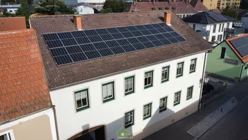Luftaufnahme eines Gebäudes mit Photovoltaikanlage auf dem Dach und traditioneller Architektur.