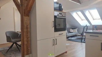 Moderne Küche mit integriertem Backofen und angrenzendem Wohnbereich unter Dachschrägen.