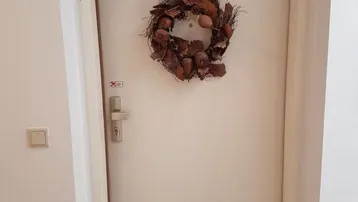Eingangstür mit herbstlichem Kranz in einem hellen Flur mit Parkettboden.