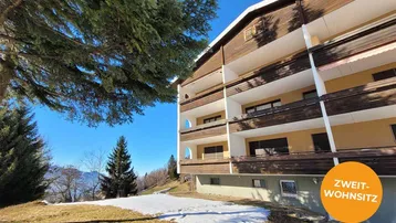 Mehrstöckiges Gebäude mit Holzfassade und Balkonen in alpiner Winterlandschaft.