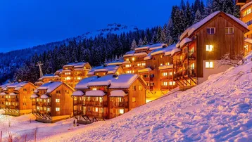 Charmante Holzchalets in verschneiter Berglandschaft bei Abenddämmerung mit beleuchteten Fenstern.