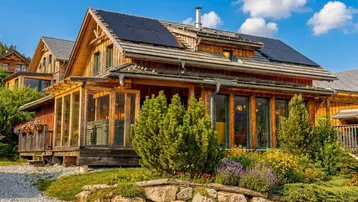 Charmantes Holzhaus mit Solarpaneelen auf dem Dach und gepflegtem Vorgarten unter blauem Himmel.