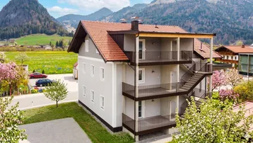Modernes Mehrfamilienhaus mit mehreren Balkonen und Bergblick in einer grünen Umgebung.