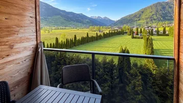 Gemütlicher Balkon mit Holzwänden, Sitzgelegenheiten und weitem Blick auf die Alpenlandschaft.