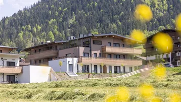 Modernes Gebäude mit Holzfassade und Balkonen, eingebettet in eine grüne Berglandschaft.