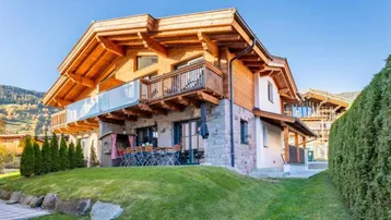 Modernes Chalet mit Steinfassade, Holzdetails, Terrasse und Garten in alpiner Umgebung.
