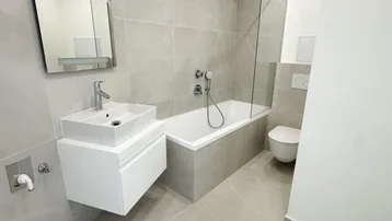 Modernes Badezimmer mit hellgrauen Fliesen, Badewanne mit Duschbereich und schwebendem Waschtisch.