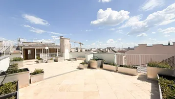 Helle Dachterrasse mit bepflanzten Metallkübeln und einem weiten Blick über die Dächer der Stadt.