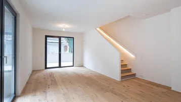 Helles, offenes Wohnzimmer mit Holzboden und moderner Treppe mit integrierter Beleuchtung.