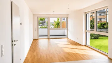 Helles, leeres Zimmer mit Parkettboden, großen Fenstern und Balkonzugang.