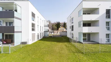Moderne Wohngebäude mit weißer Fassade und einem gepflegten Gemeinschaftsgarten in sonniger Lage.