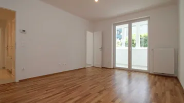 Helles Zimmer mit Parkettboden und Zugang zu einem kleinen Balkon, ideal als Wohn- oder Schlafbereich.