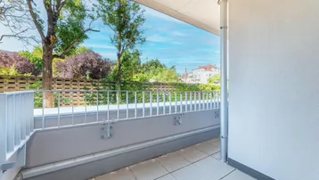 Heller Balkon mit Fliesenboden und Blick ins Grüne, umgeben von Bäumen.