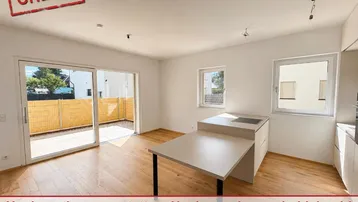 Heller offener Wohnbereich mit Holzboden, moderner Küchenzeile und Zugang zu einer Terrasse.