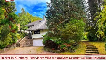 Villa aus den 70er Jahren mit großem Grundstück, umgeben von viel Grün und Bäumen.