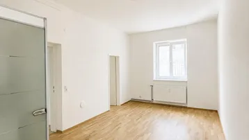 Helles, modernisiertes Zimmer mit Parkettboden, weißen Wänden und einem Fenster, das viel Tageslicht hereinlässt.