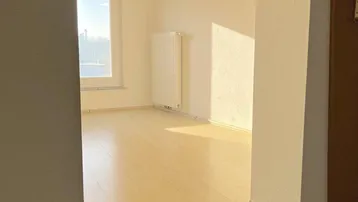 Helles Zimmer mit Holzfußboden und Fenster, das viel Sonnenlicht hereinlässt.