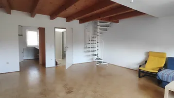 Geräumiges Wohnzimmer mit sichtbaren Holzbalken, Parkettboden und einer Wendeltreppe zum oberen Bereich.