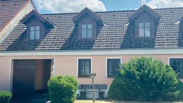 Traditionelles Gebäude mit Dachgauben und rosa Fassade unter blauem Himmel.