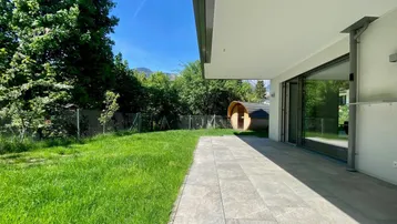 Große gepflasterte Terrasse mit Rasenfläche und einem Fasssauna im Gartenbereich.