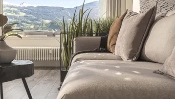 Helles Wohnzimmer mit beigem Sofa, Holzboden und beeindruckendem Bergblick durch große Fenster.