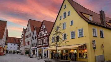 Historische Gebäude in einer malerischen Altstadtgasse mit einem gelben Haus im Vordergrund und einem bunten Himmel.