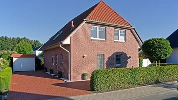 Klassisches Einfamilienhaus mit rotem Ziegeldach, Klinkerfassade und gepflegter Hecke im Vorgarten.