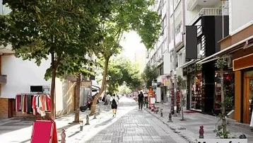 Belebte Stadtstraße mit Geschäften, Bäumen und Fußgängern, die das urbane Umfeld der Immobilie zeigt.