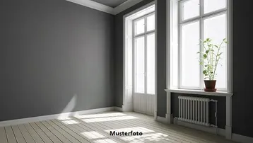 Heller Raum mit grauen Wänden, hellen Holzdielen und großen Fenstern, die viel Tageslicht hereinlassen.