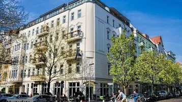 Elegantes Eckgebäude in städtischer Umgebung mit klassischen Balkonen und Geschäften im Erdgeschoss.