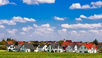 Reihenhäuser in einer ländlichen Umgebung mit grünen Feldern und blauem Himmel.
