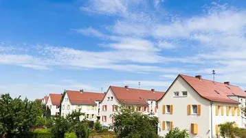 Reihenhäuser mit roten Ziegeldächern und gelben Fensterläden unter blauem Himmel.
