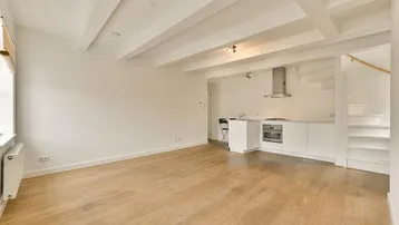 Heller Wohnbereich mit offener Küchenzeile, Holzbalkendecke und Parkettboden sowie einer Treppe.