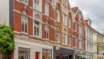 Historische Backsteinfassade mit dekorativen Elementen und Geschäften im Erdgeschoss an einer Stadtstraße.