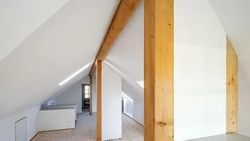 Heller Dachbodenraum mit sichtbaren Holzbalken und schrägen Wänden, bereit für den Ausbau.