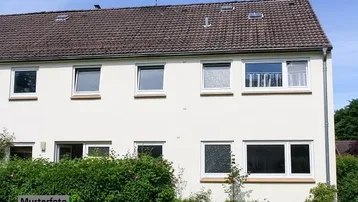 Außenansicht eines Wohngebäudes mit heller Fassade, Satteldach und grüner Bepflanzung im Vordergrund.